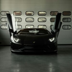 A stunning black luxury car with open gullwing doors, parked in a sleek garage setting.